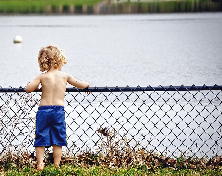 boy, leaning, gray, metal fence, lake, kid, young, water, watching, serious