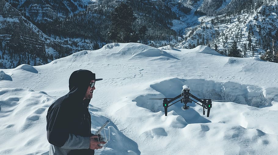 man, wearing, pull-over jacket infront, black, quadcopter, snow field mountain, pull, jacket, infront, snow field