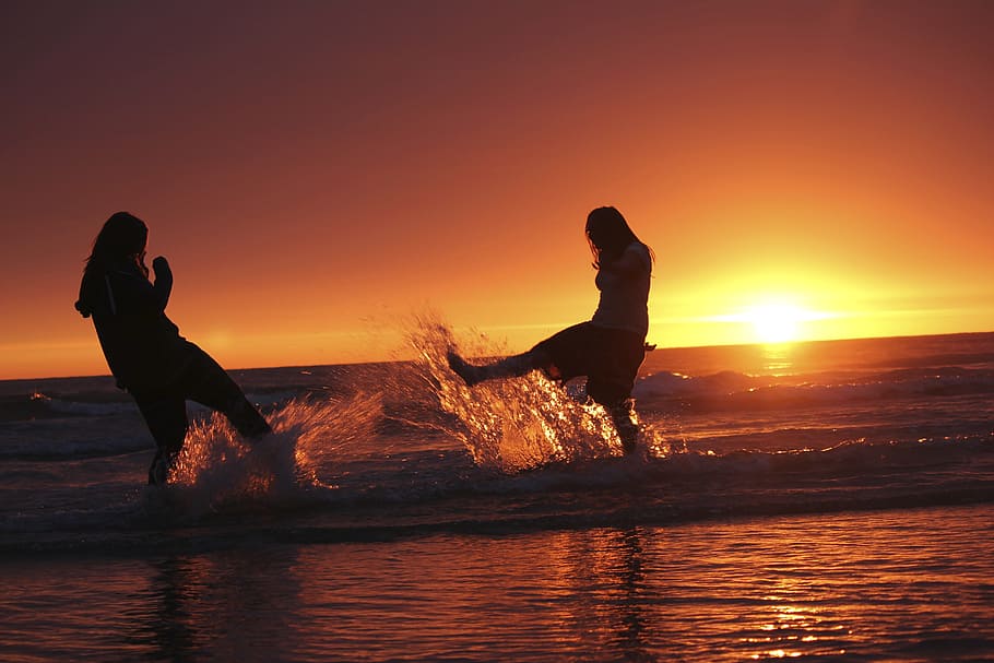silhueta, dois, meninas, jogando, beira-mar, chutando, agua, Pôr do sol, batalha na água, amigos