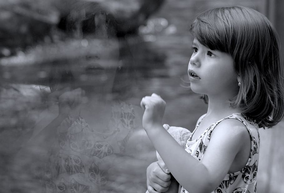 grayscale photo, girl, standing, next, clear, glass panel, emotion, expresion, child, expression