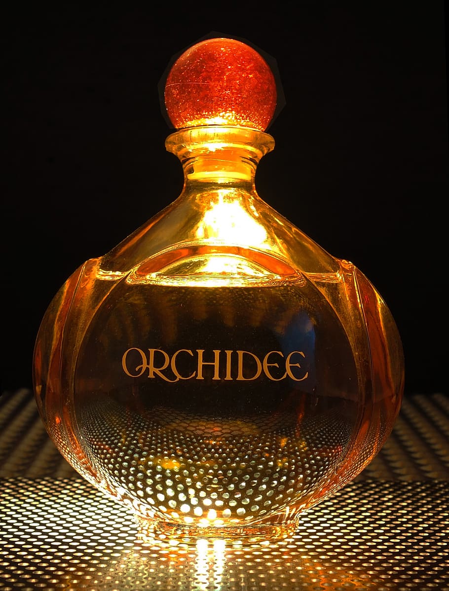 orange, orchidee glass fragrance bottle, perfume, bottle, light from below, indoors, illuminated, black background, communication, western script