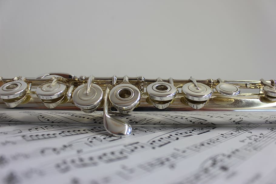 silver wind instrument, music, flute, instrument, musical instrument, paper, sheet music, indoors, arts culture and entertainment, wind instrument
