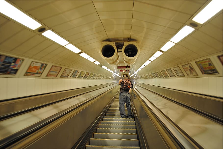 escalator, subway station, guy, backpack, knapsack, indoors, illuminated, transportation, travel, moving walkway