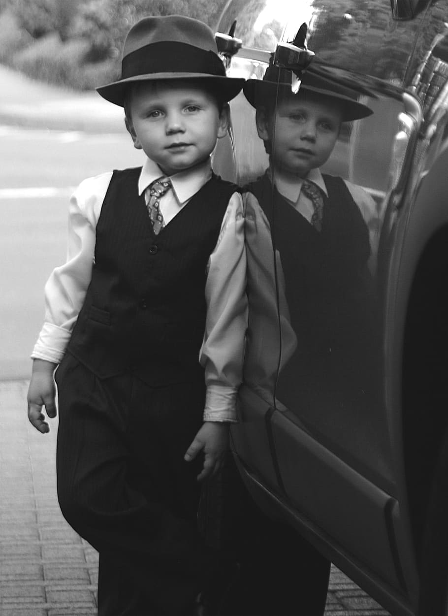 grayscale photography, boy, dress shirt, vest, fedora hat, leaning, car, grayscale, semi-formal, suit