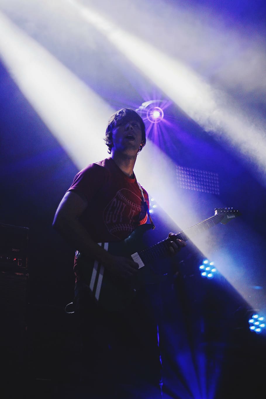 man, wearing, red, crew-neck shirt, playing, electric, guitar, stage, stage lights, turned