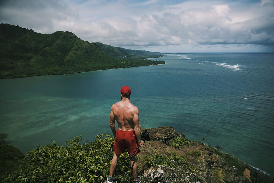 man, standing, cliff, surrounded, water, daytime, red, shorts, high, ground