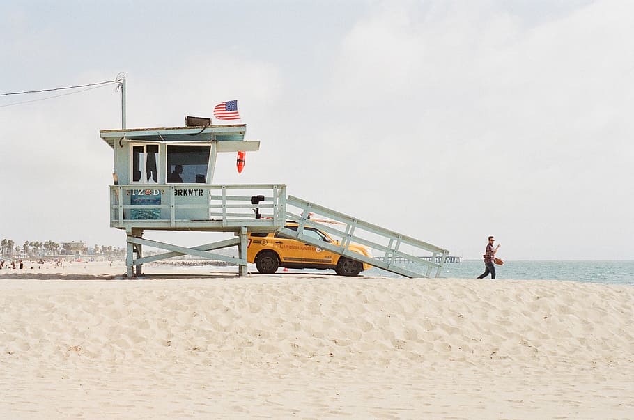 person, walking, beach, dessert, daytime, sand, lifeguard, truck, suv, flag