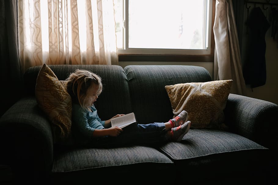 child, sitting, couch infront, window, kid, people, girl, couch, pillow, reading
