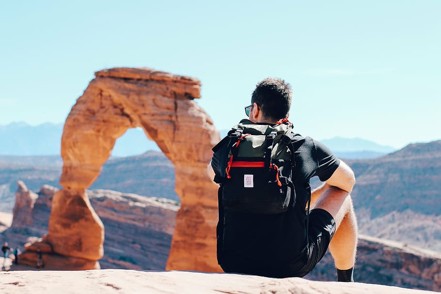 man, wearing, hydropack backpack, sitting, hill, facing, delicate, arch, utah, gray