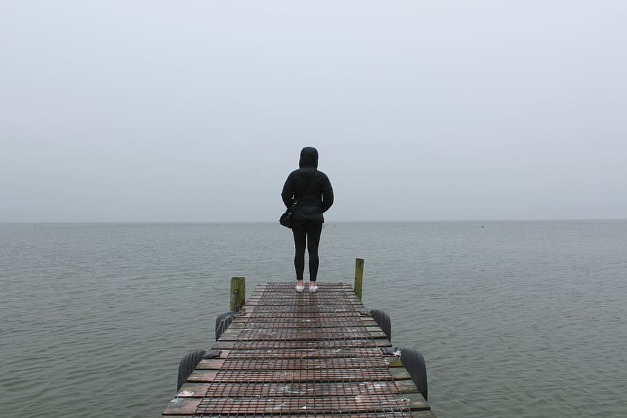 person, standing, dock, daytime, woman, black, hoodie, brown, wooden, near