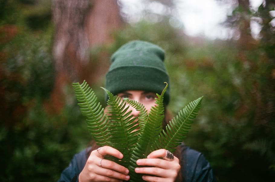 woman, wearing, green, knit, cap, black, top, holding, fern plant, selective