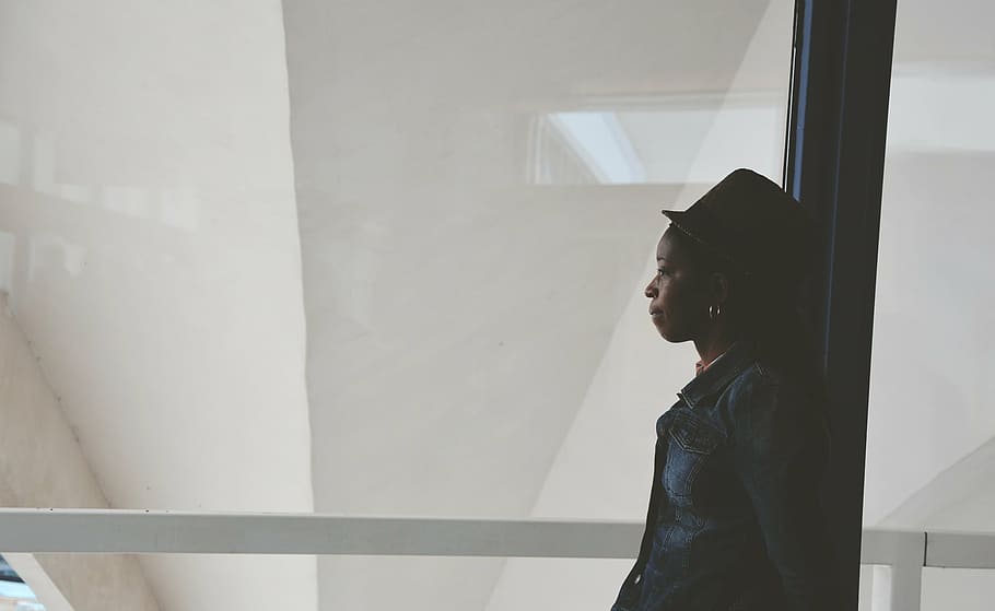 mulher, vestindo, boné, em pé, ao lado de, parede de painel de vidro, africano, americano, chapéu, afro-americano