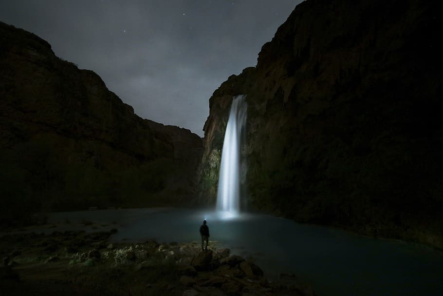 person, standing, alone, rock, facing, lighted, waterfall, night time, nature, landscape