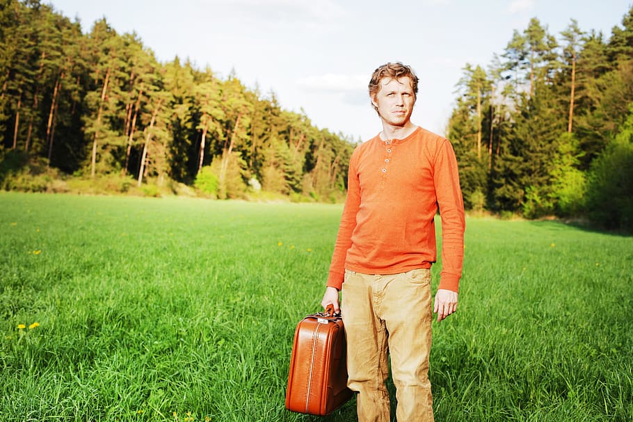 man, orange, half-button, long-sleeved, brown, denim jeans, carrying, suitcase, standing, green