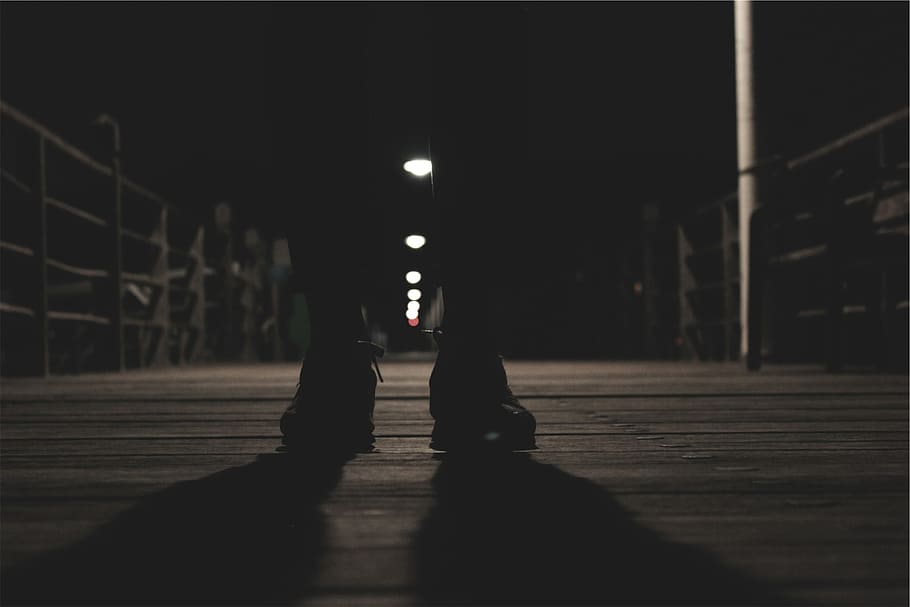 silhouette photo, person, standing, bridge, front, railed, post lights, shoes, dark, shadows
