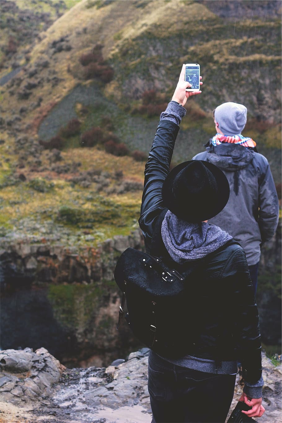person, raising, hand, holding, smartphone, taking, man, standing, cliff, daytime