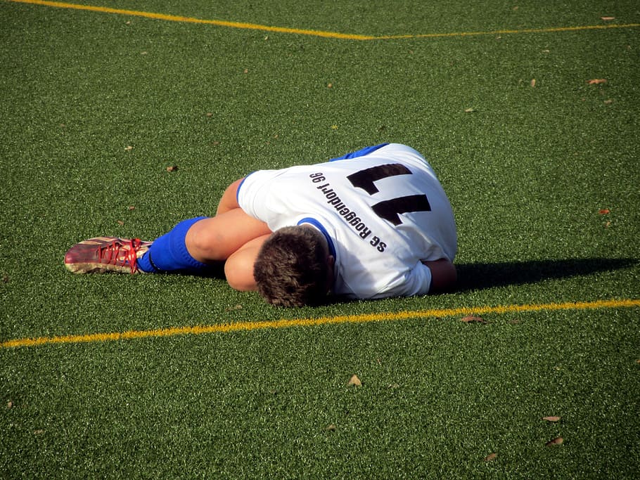 man, wearing, white, black, soccer uniform, lying, green, grass field, football, injury