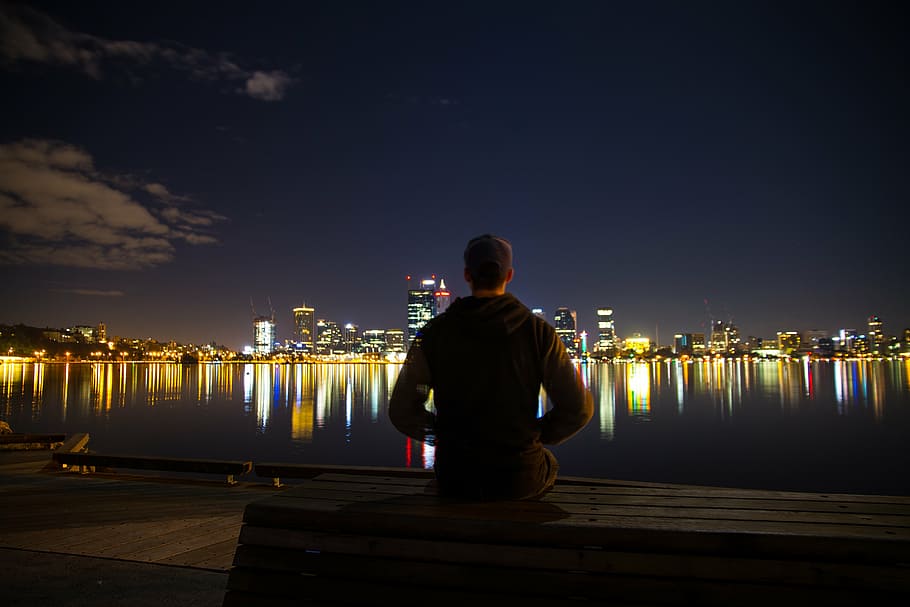man, standing, lake, watching, city shoreline lights, night time, gray, jacket, sitting, near