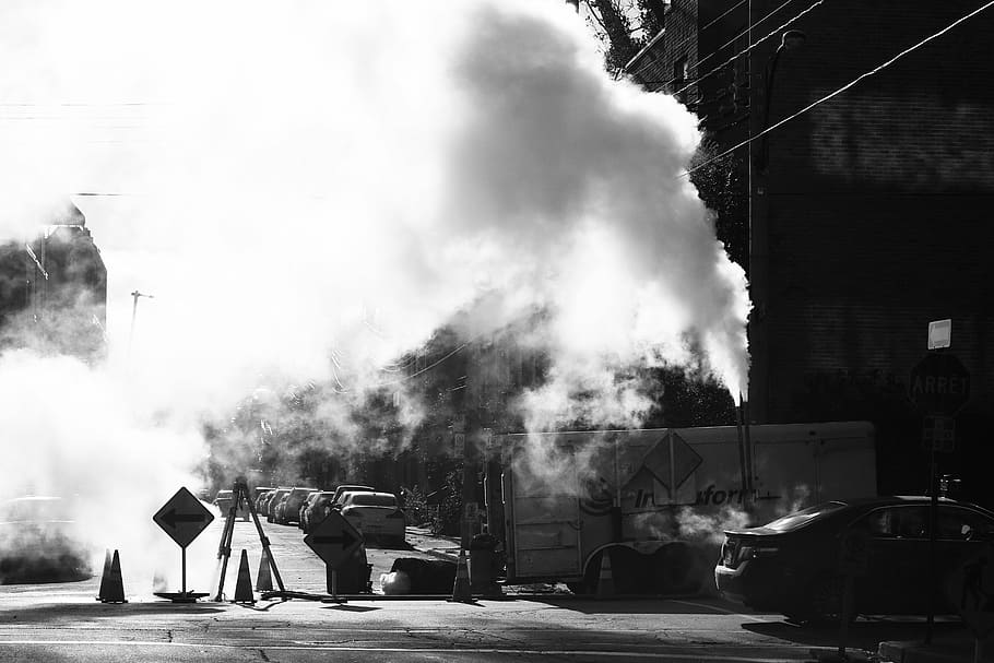 grayscale photo, smoke, construction, signs, pylons, street, road, block, cars, smoke - physical structure