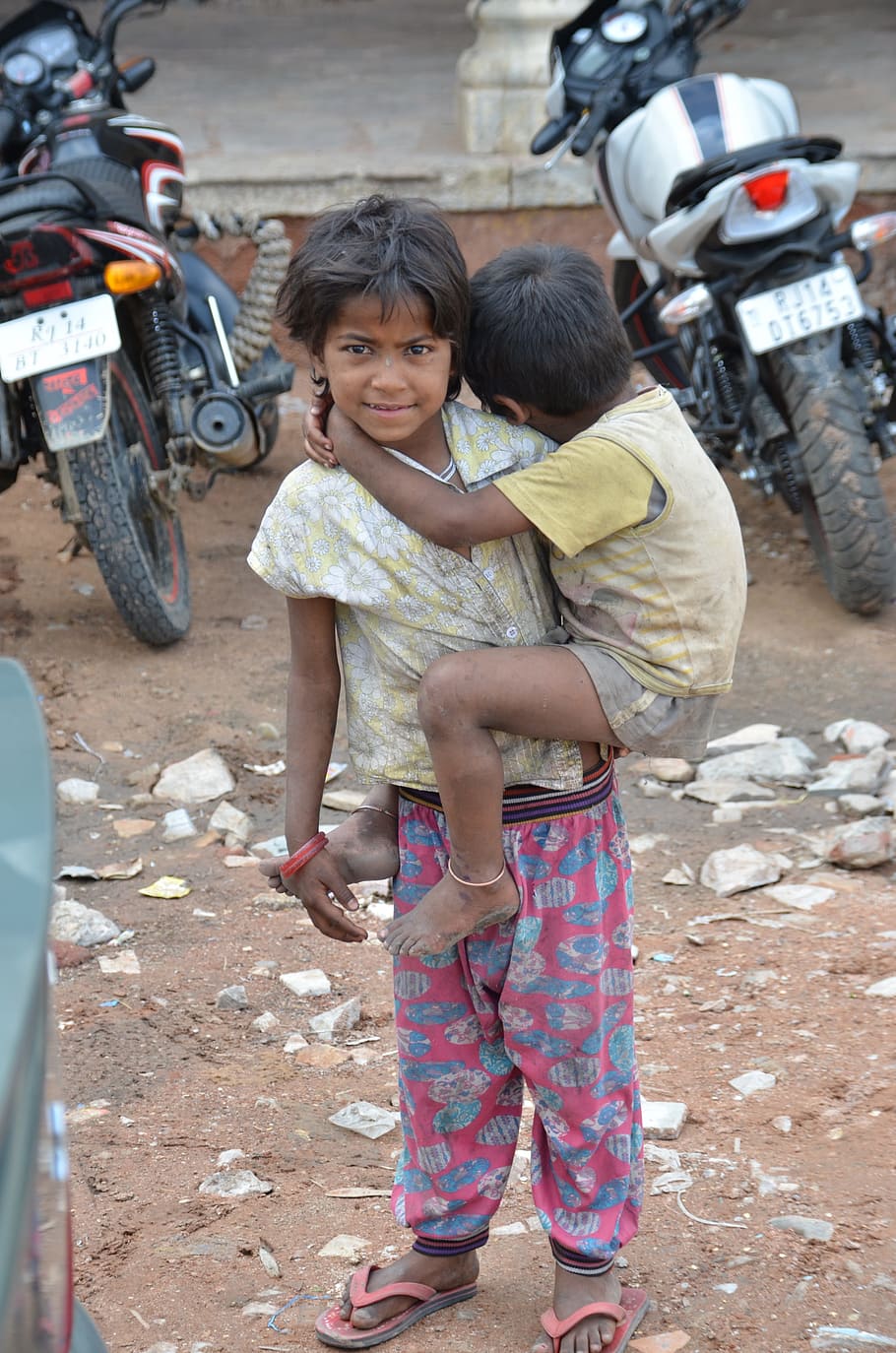 child, carrying, toddler, standing, parked, motorcycles, daytime, brothers, poverty, begging