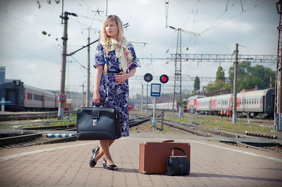 woman, blue, white, floral, elbow-sleeved dress, holding, black, leather handbag, daytime, station