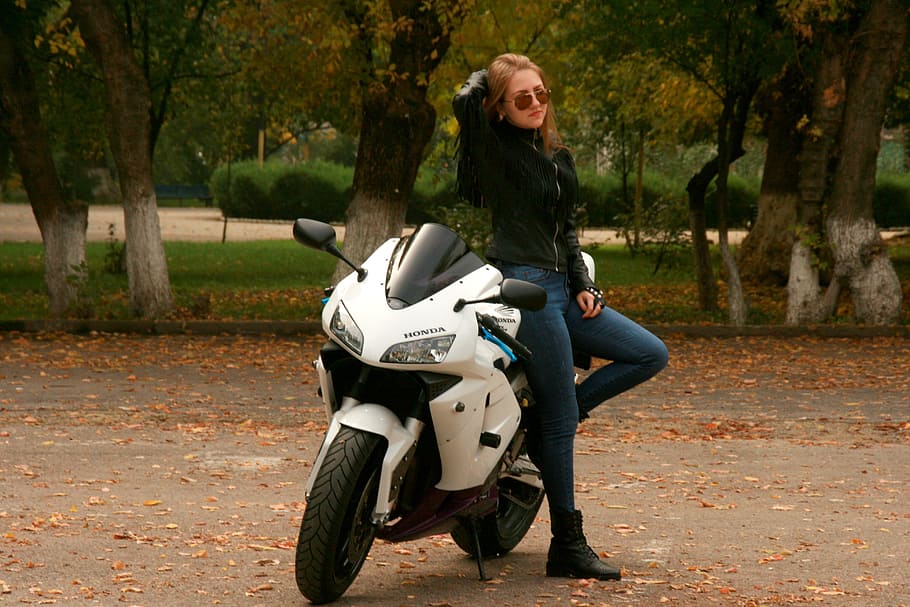 woman, wearing, blue, fitted, jeans, black, zip-up jacket, standing, white, honda sportsbike
