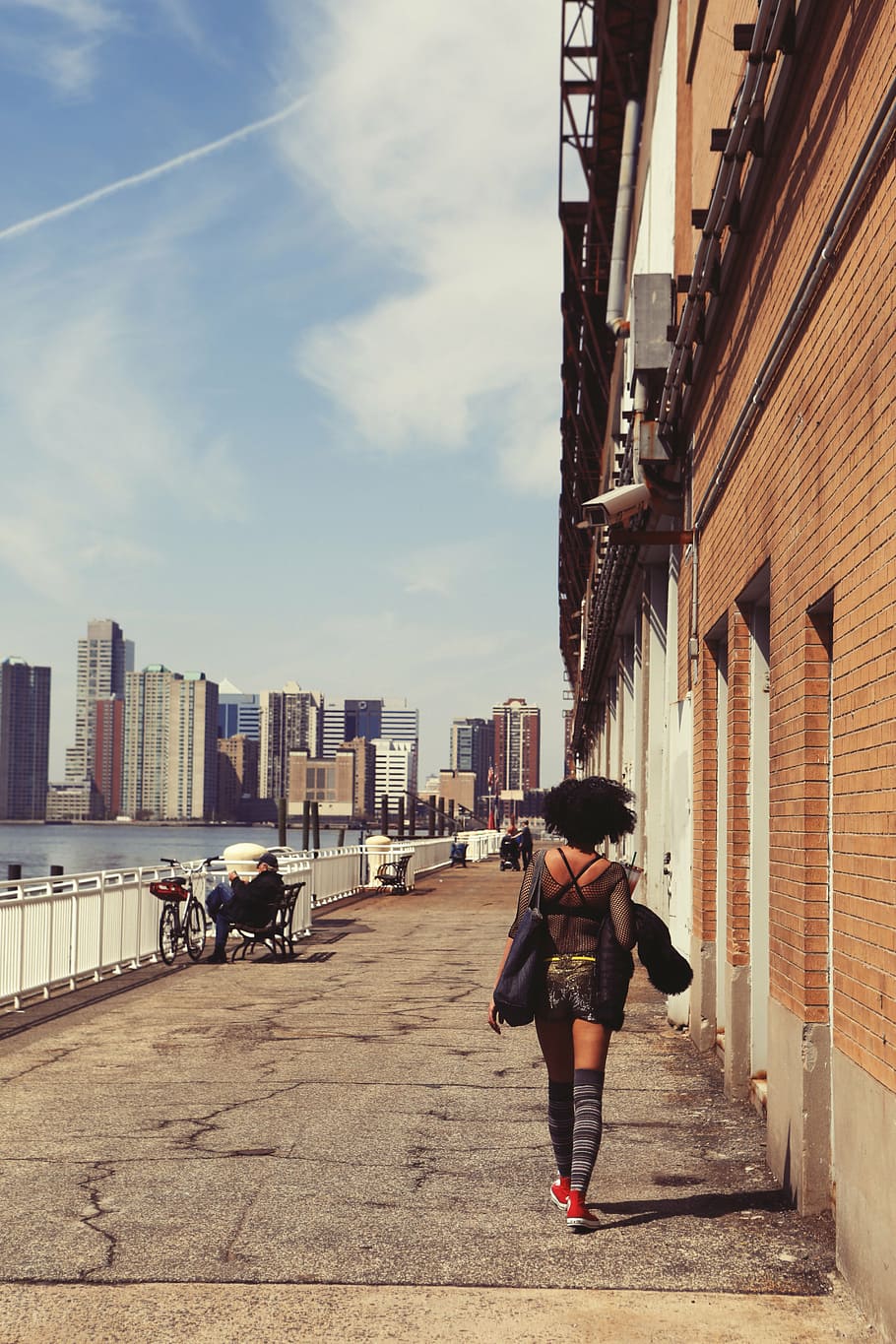 woman, walking, building, surveillance camera, black, dress, alongside, brown, brick, wall