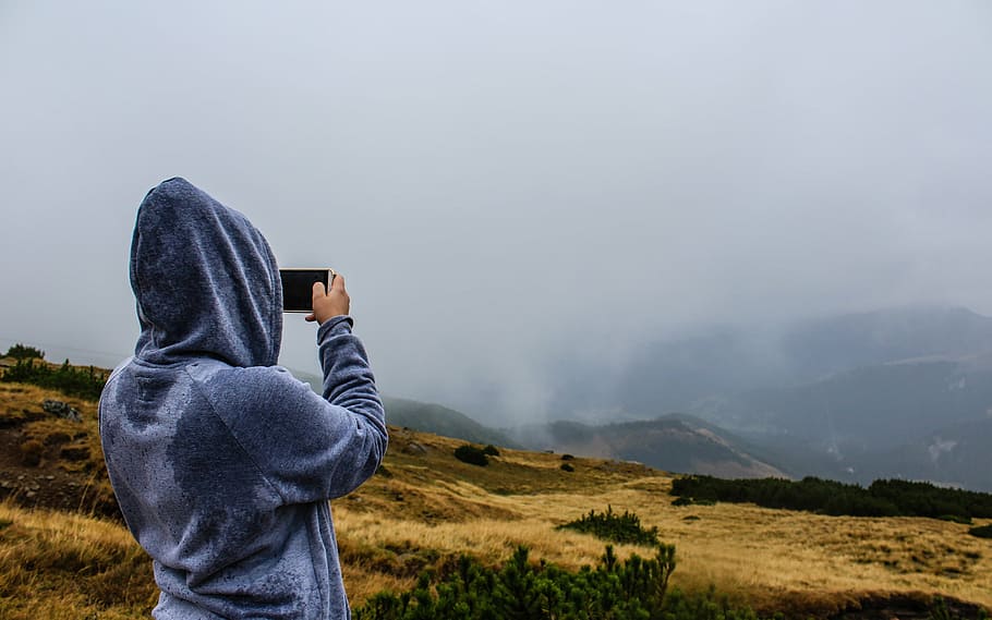 person, holding, black, smartphone, taking, picture mountain, people, hoodie, outdoors, nature