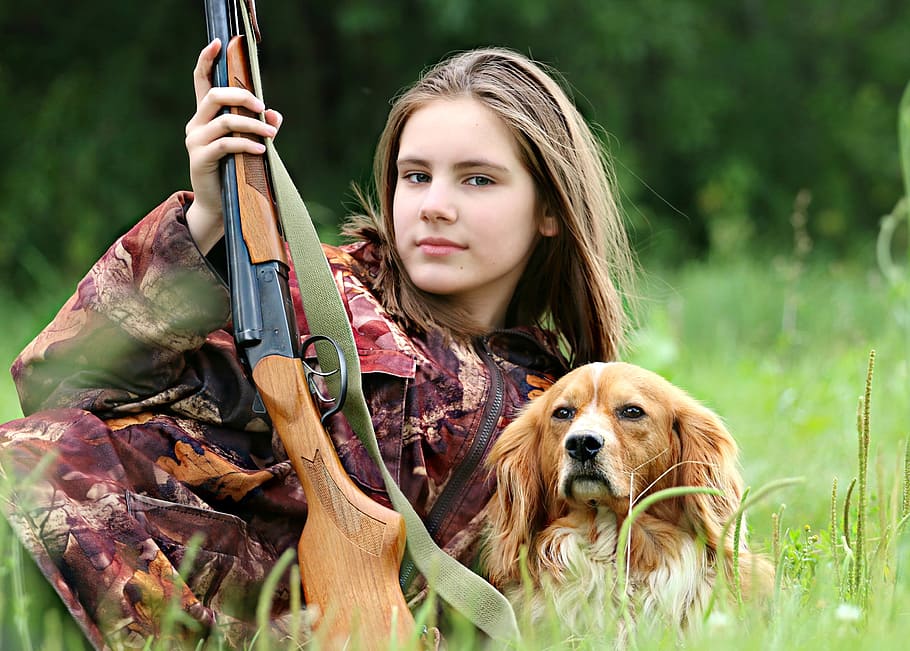 woman, red, tree camouflage suit, holding, brown, hunting rifle, orange, white, welsh springer spaniel, grass field