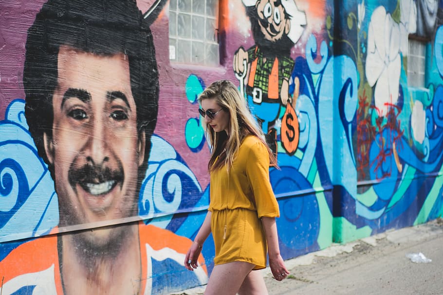 mulher, andando, ao lado, parede, grafite, vestindo, amarelo, macacão, vestir, rua