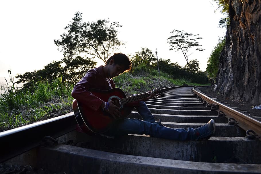 man, playing, guitar, sitting, train rail, daytime, railroad, guitarist, boy, pose