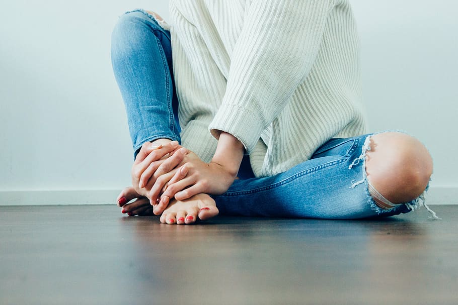 person, holding, right foot, wearing, distressed, jeans, woman, girl, lady, people