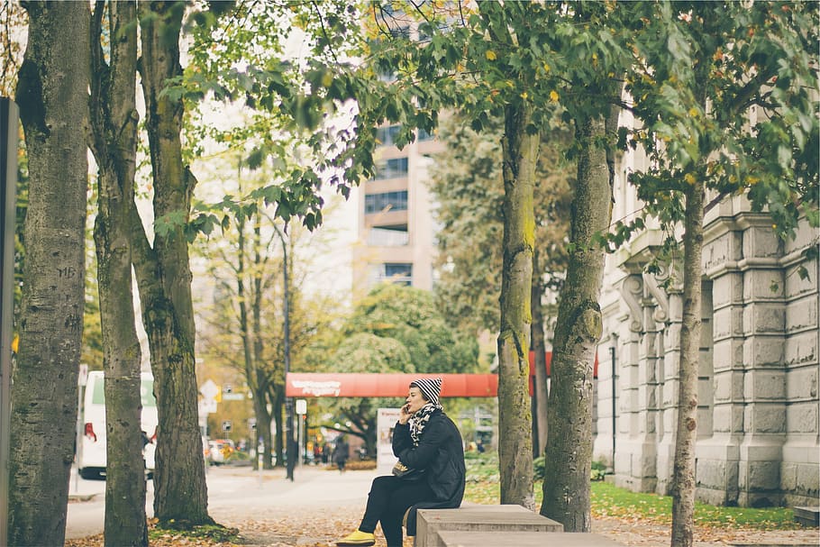 mulher, falando, telefone celular, banco, sentado, calçada, cidade, chapéu, jaqueta, árvores