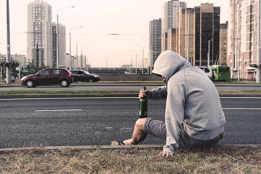 man, wearing, hoodie, sitting, road, holding, bottle, cars, day, on the street