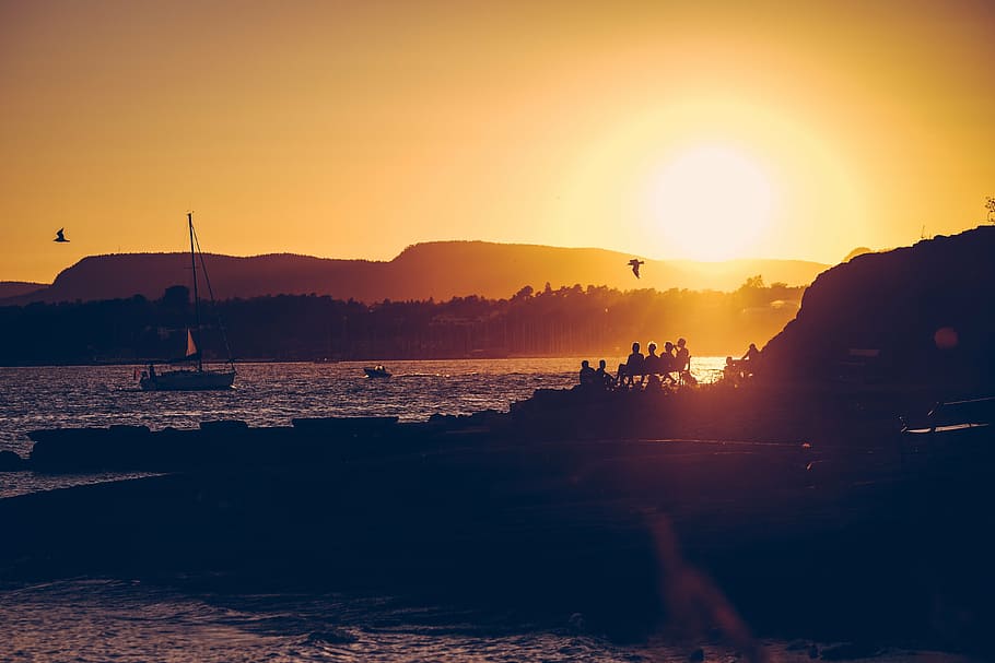 fotografía de silueta, gente, sentado, banco, mirando, playa, vela, barco, puesta de sol, anochecer