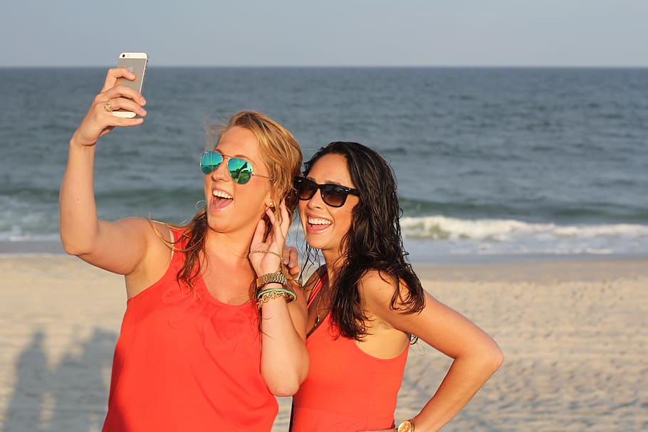 two, woman, wearing, red, tank tops, taking, photos, white, sand beach shore, two women
