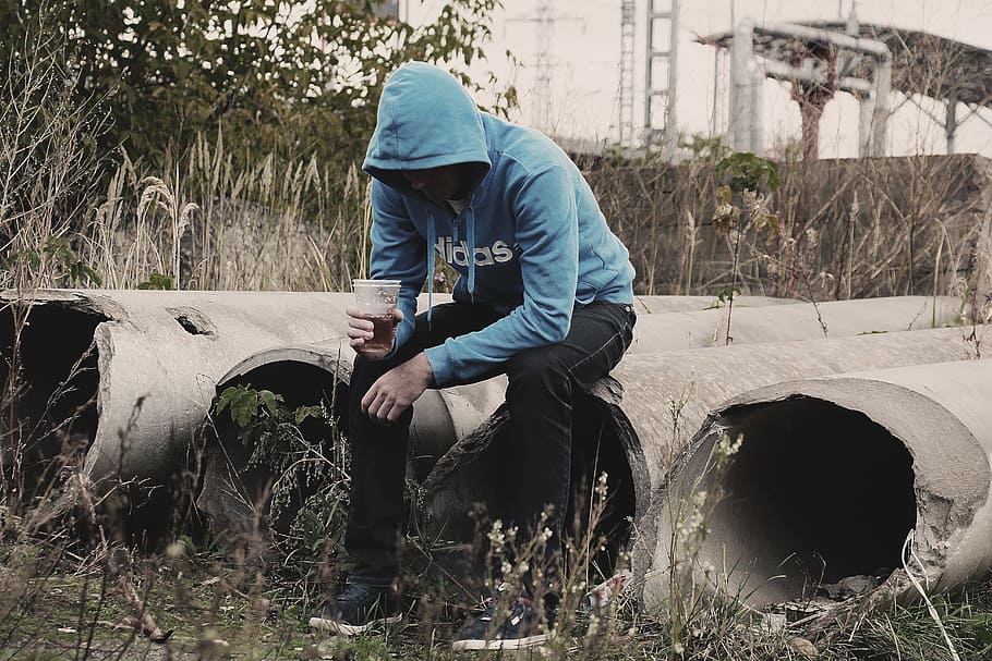 man, wearing, black, pants, blue, adidas pullover hoodie, sitting, gray, concrete, poles
