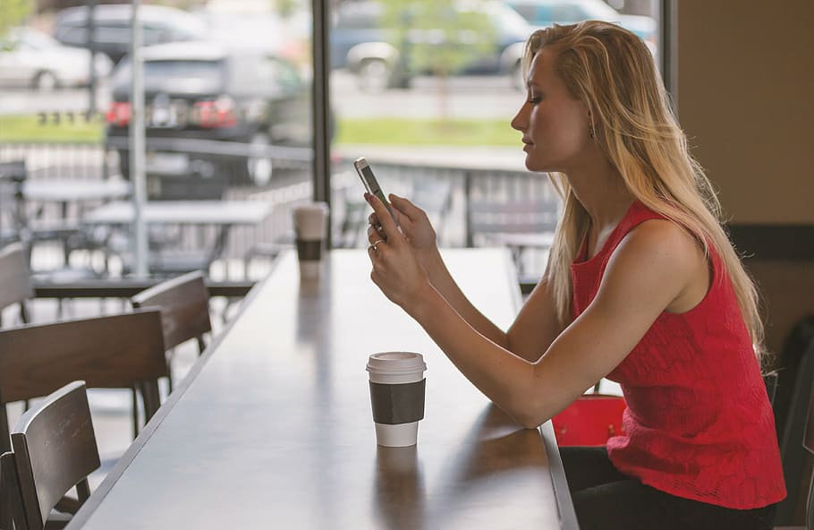 woman, wearing, red, sleeveless shirt, sitting, counter, phone, smartphone, female, coffee