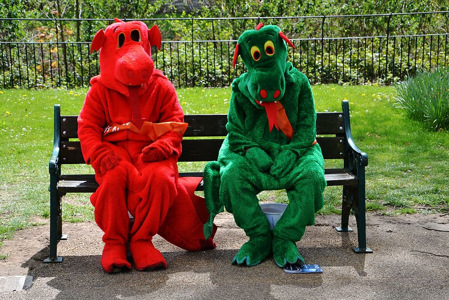 two, person, wearing, red, green, dinosaur mascots, sitting, black, wooden, bench
