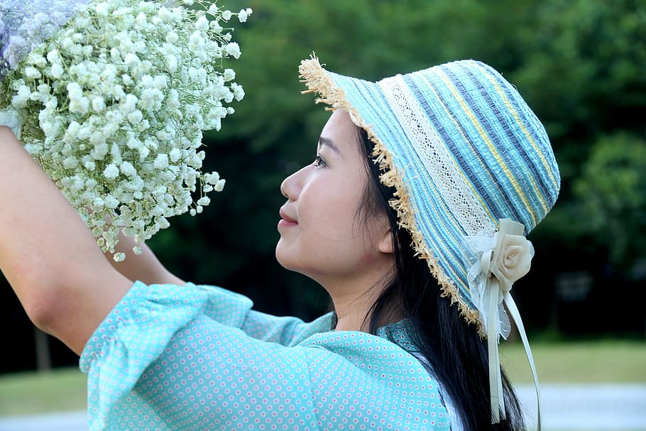 woman, wearing, teal, top, striped, hat, holding, white, cluster flowers, shot from the side