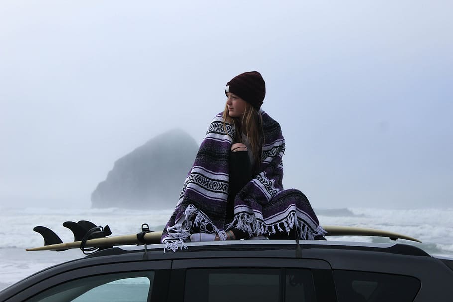 woman, blanket, sitting, surfboard, top, vehicle, sea, distant, mountain isle, standing