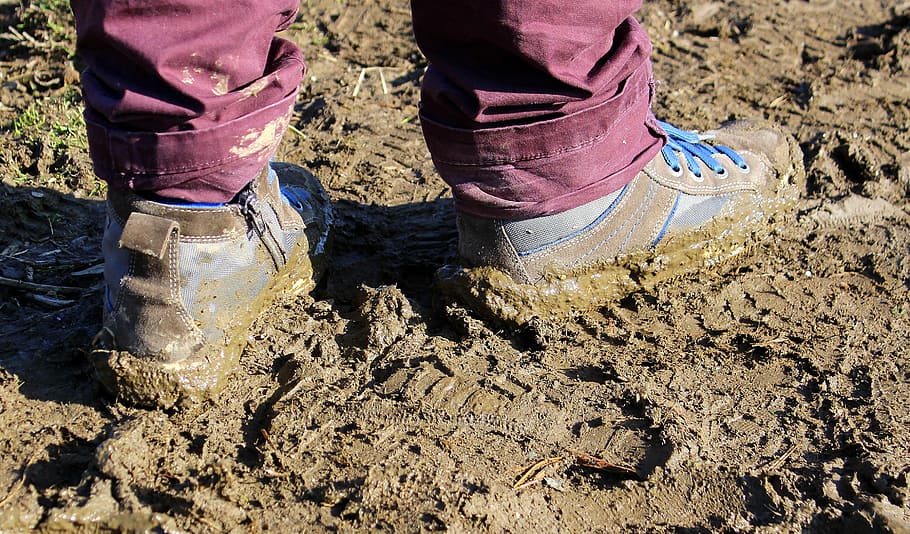 person, wearing, blue, low-top sneakers, standing, mud, daytime, earth, wet earth, ground