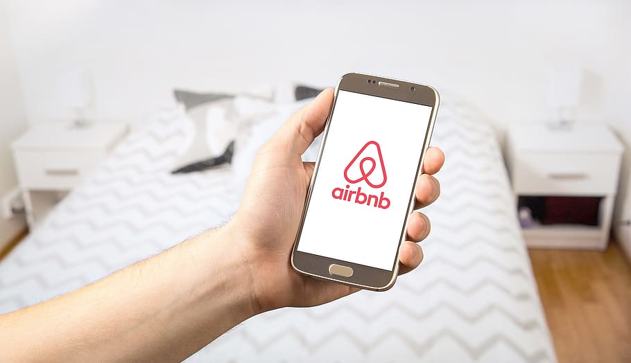 person, holding, smartphone, displaying, airbnb logo, airbnb, apartment, rental, logo, holiday