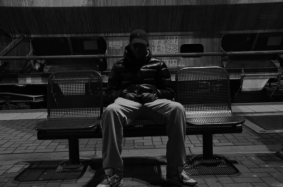 grayscale view, man, sitting, gang bench, young, guy, hat, jacket, pants, chairs