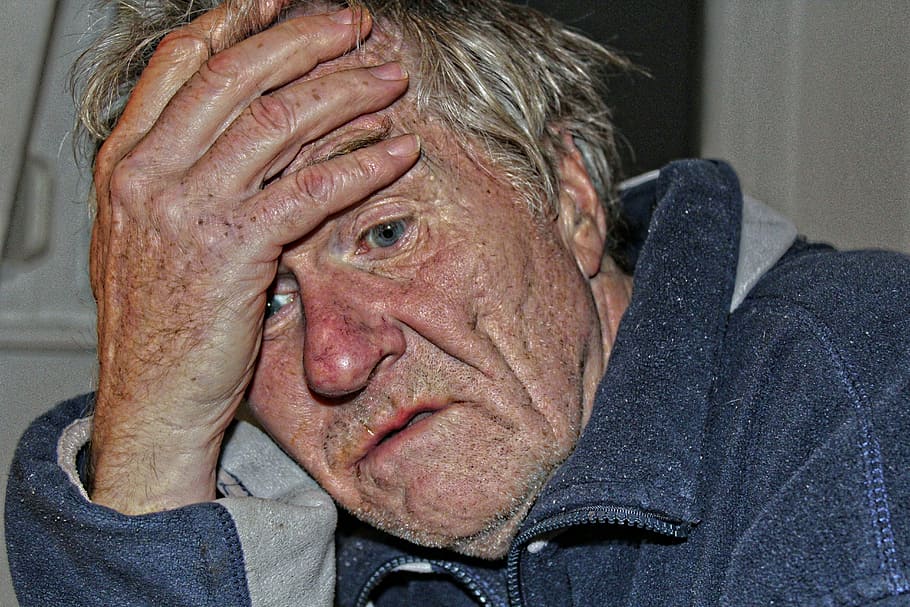 An older adult sitting down with his head in his hand with a confused/worried look on his face.