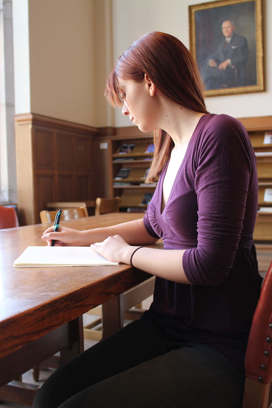 woman, wearing, purple, v-neck shirt siting, table, writing, long, sleeve, top, notebook