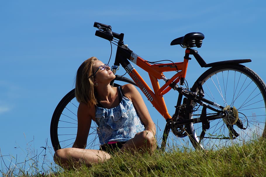 woman, sitting, green, grasses, orange, black, full-suspension bicycle, daytime, sunbathing, round