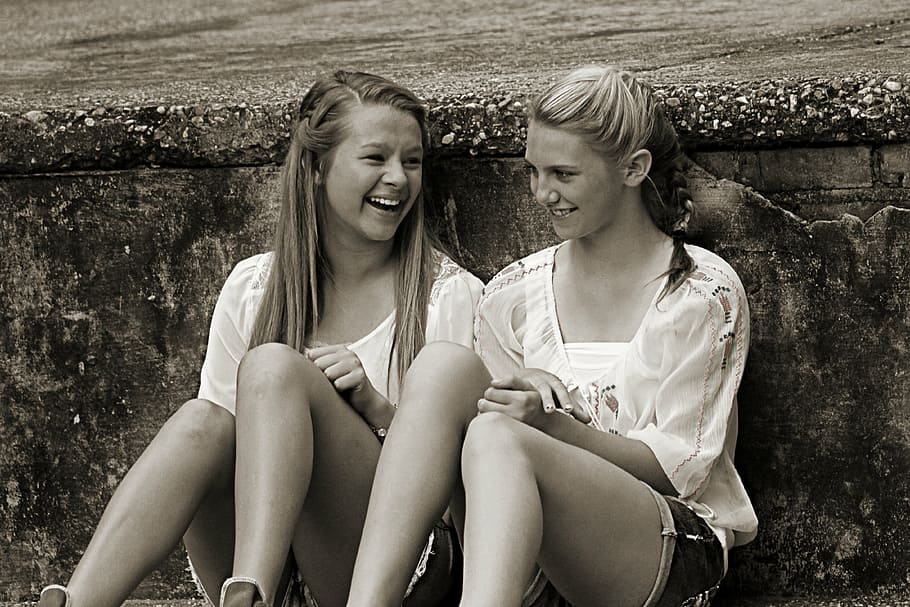 two, girls, sitting, leaning, wall, young, happy, friends, smiling, together