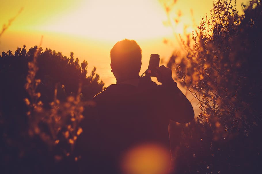 man, standing, holding, dslr camera, right hand, Sunset, Summer, silhouette, rear view, photographing