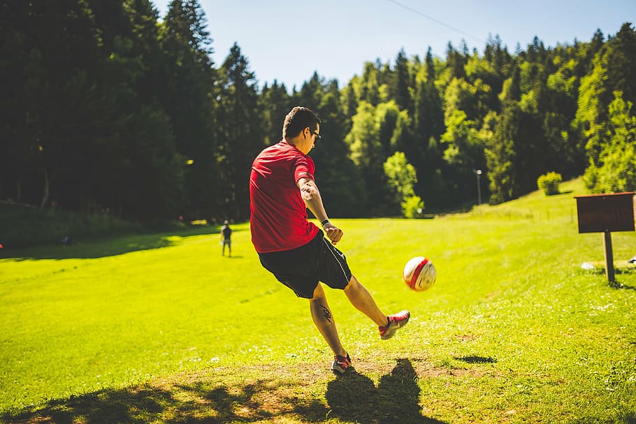 hombre, jugando, fútbol, ​​verde, campo de hierba, rojo, camiseta, césped, campo, tiempo de día